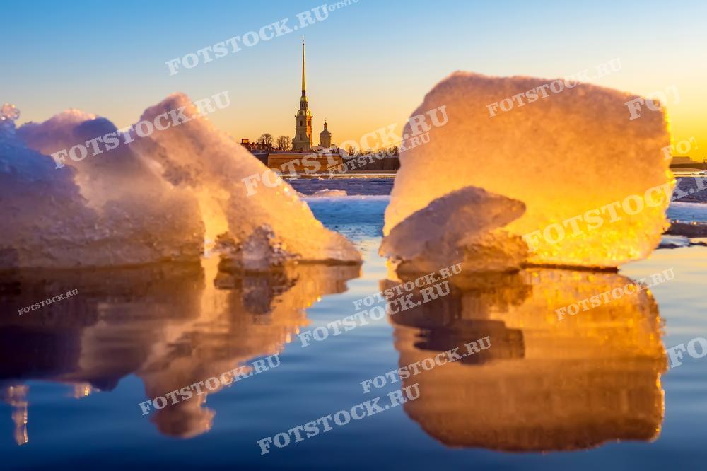 Куски льда на переднем плане фотографии красиво отражаются в водах Невы, создавая почти зеркальное изображение, которое в сочетании с тёплым светом утреннего солнца придаёт сцене мирную и вдохновляющую атмосферу. Петропавловская крепость на заднем плане узнаваема благодаря своему историческому силуэту и золотому шпилю. Это фото может быть использовано в качестве иллюстративного материала для туристических путеводителей, в статьях об отдыхе в России и как красивый пример природной фотографии.